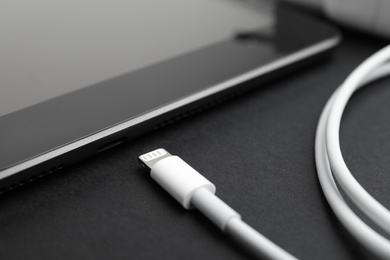 Photo of Tablet and USB charge cable on black background, closeup. Modern technology