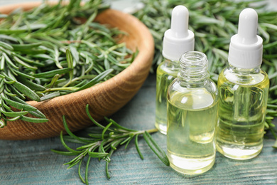 Photo of Fresh rosemary and bottles of essential oil on light blue wooden table