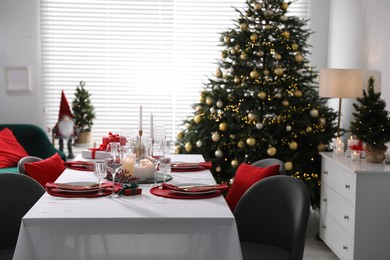 Christmas table setting with burning candles, gift box and dishware in room