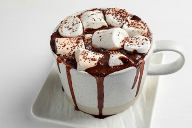 Delicious hot chocolate with marshmallows and cocoa powder in cup on white table, closeup