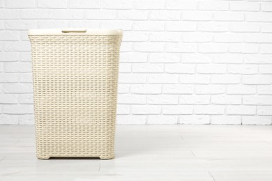 Photo of Empty laundry basket near white brick wall. Space for text
