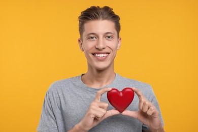 Photo of Happy man holding red heart on orange background