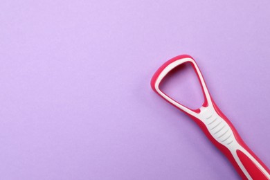 Photo of Red tongue cleaner on violet background, top view. Space for text