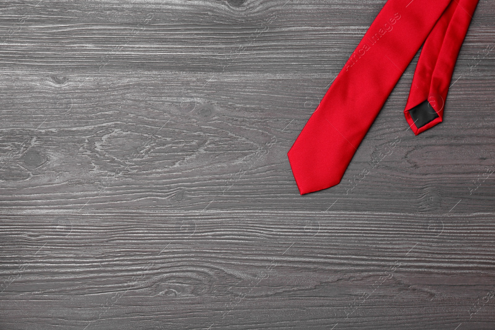 Photo of Stylish red silk necktie on dark grey wooden table, top view with space for text