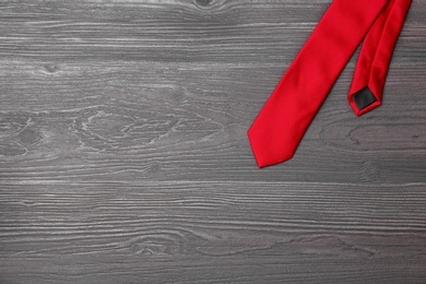 Photo of Stylish red silk necktie on dark grey wooden table, top view with space for text