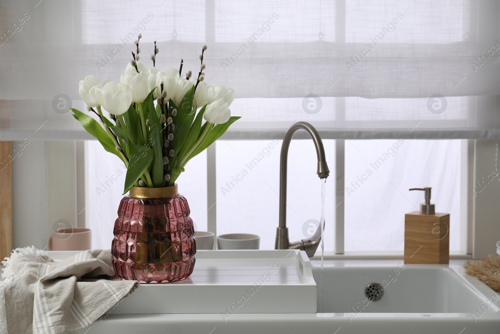 Photo of Beautiful bouquet of willow branches and tulips in vase near sink, space for text