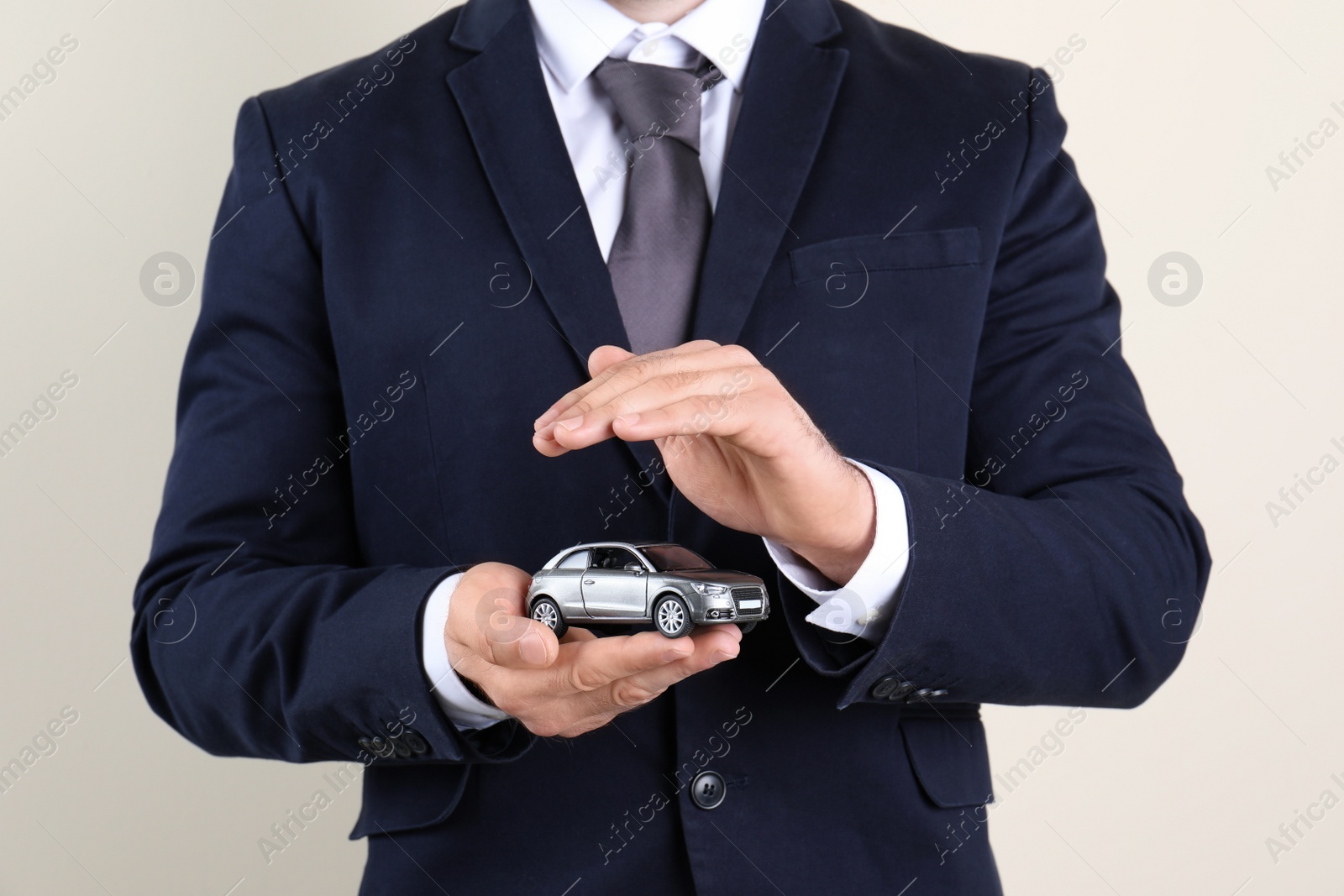 Photo of Male insurance agent holding toy car on light background, closeup