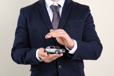 Male insurance agent holding toy car on light background, closeup