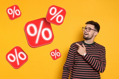 Image of Discount offer. Happy man pointing at falling cubes with percent signs on orange background
