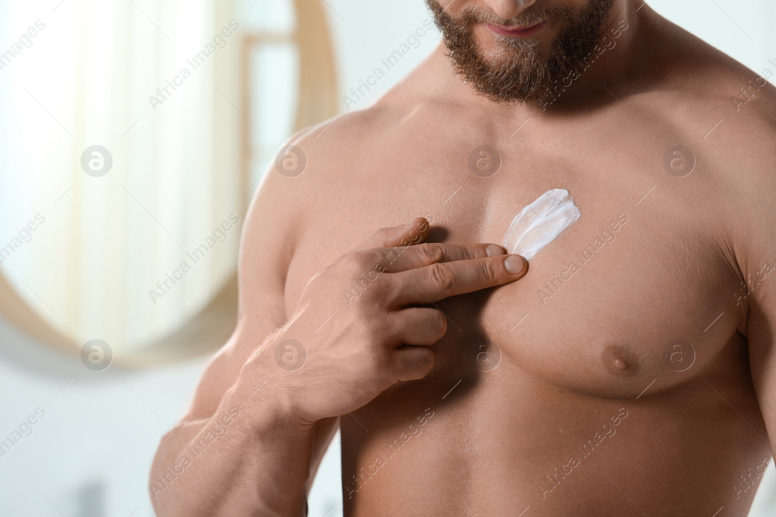 Photo of Man applying body cream onto his chest in bathroom, closeup