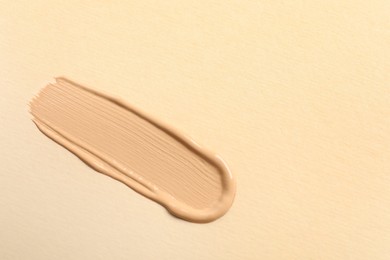 Photo of Smear of skin foundation on beige background, top view. Space for text