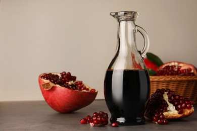 Photo of Glass jug of tasty pomegranate sauce and fresh ripe fruits on light grey table. Space for text