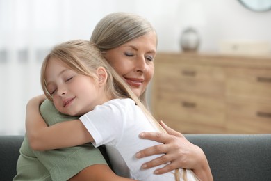 Happy grandmother hugging her granddaughter at home, space for text