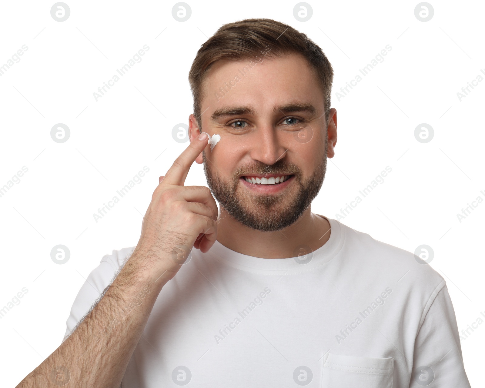 Photo of Happy young man applying facial cream on white background