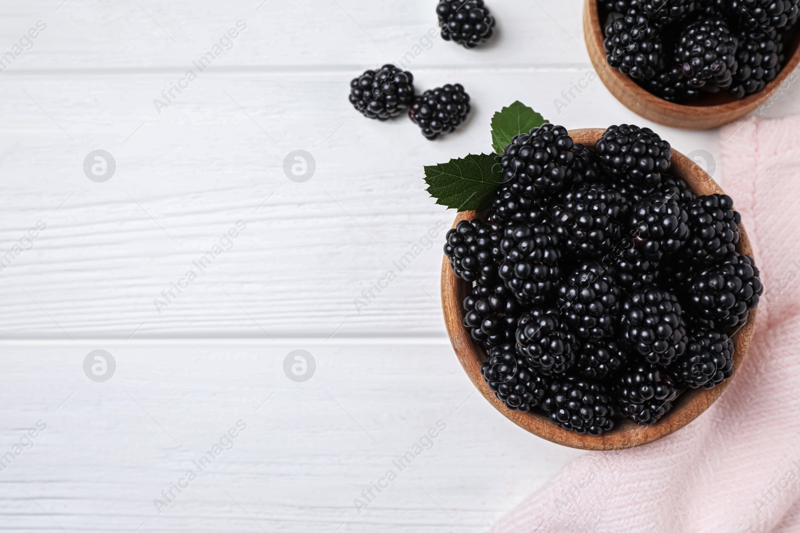 Photo of Fresh ripe blackberries in bowls on white wooden table, flat lay. Space for text