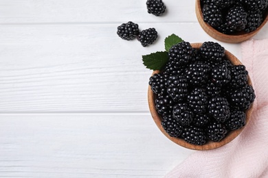 Photo of Fresh ripe blackberries in bowls on white wooden table, flat lay. Space for text