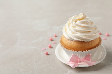 Photo of Delicious cupcake decorated with cream and bow on light grey table, space for text