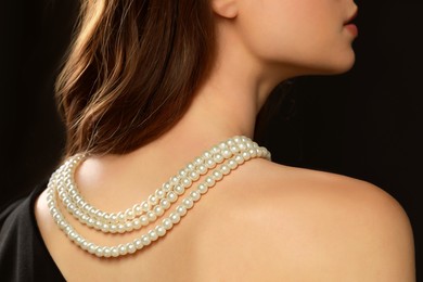 Photo of Young woman wearing elegant pearl necklace on black background, closeup