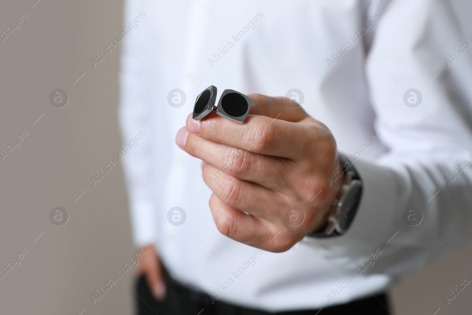 Photo of Stylish man holding cufflinks against beige background, closeup