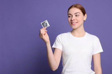 Woman holding condom on purple background, space for text. Safe sex