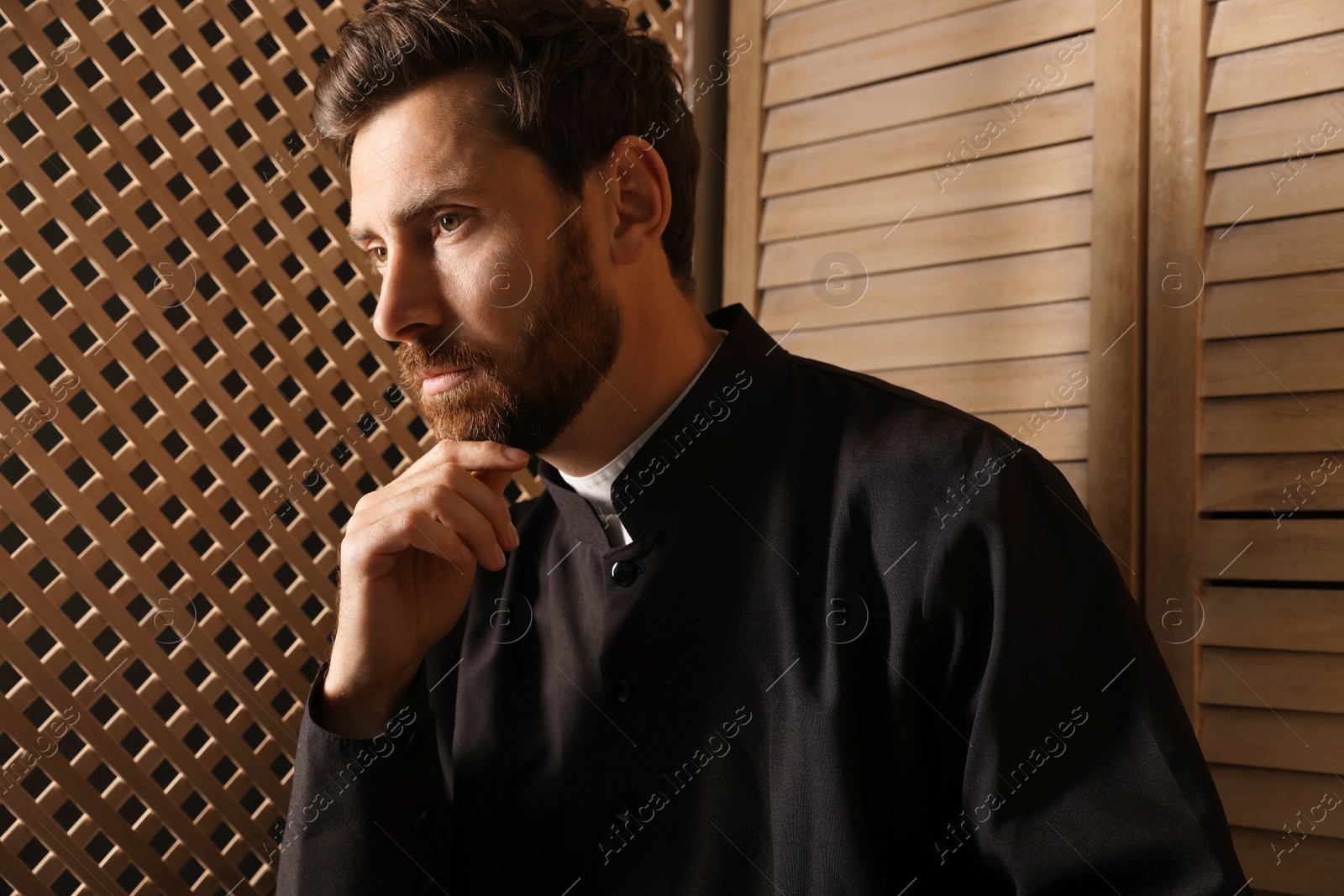 Photo of Catholic priest wearing cassock in confessional booth