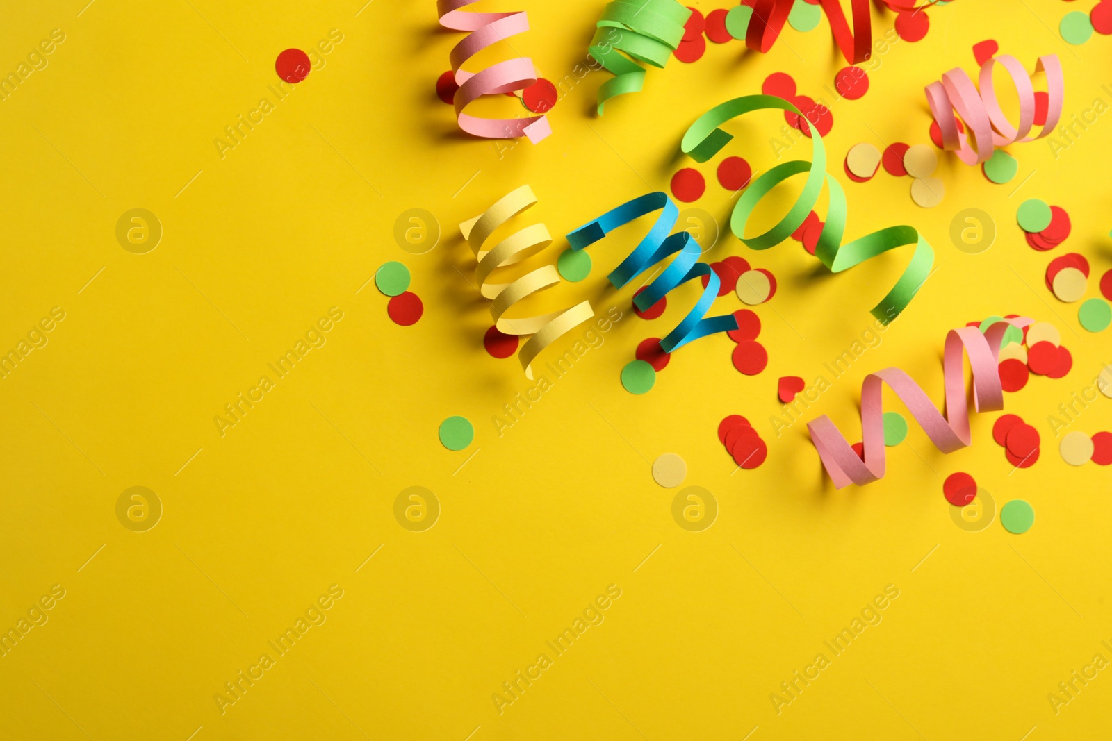 Photo of Colorful serpentine streamers and confetti on yellow background, flat lay. Space for text