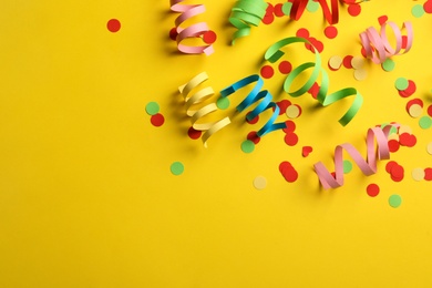 Colorful serpentine streamers and confetti on yellow background, flat lay. Space for text