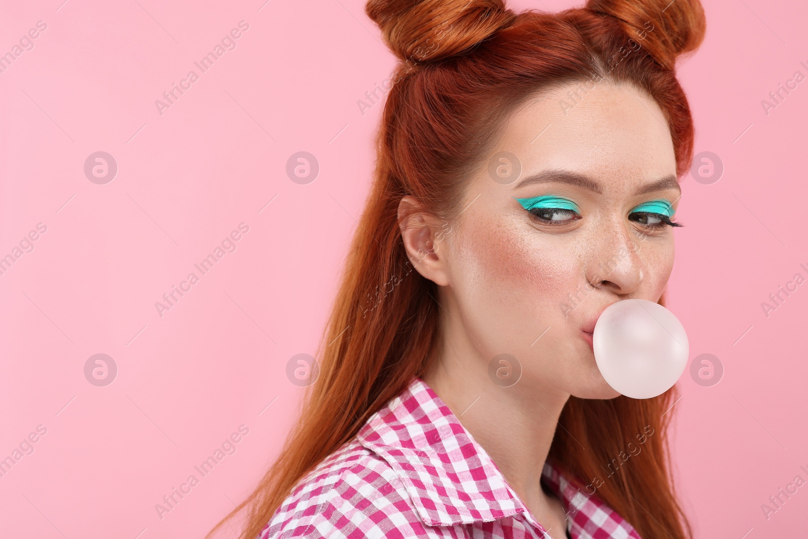 Photo of Beautiful woman with bright makeup blowing bubble gum on pink background. Space for text