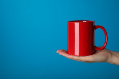 Photo of Woman holding red mug on light blue background, closeup. Space for text