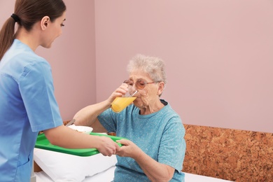 Photo of Nurse giving food to senior woman in hospital ward