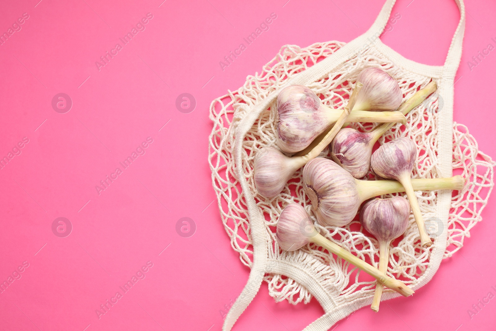Photo of String bag with garlic heads on bright pink background, top view. Space for text