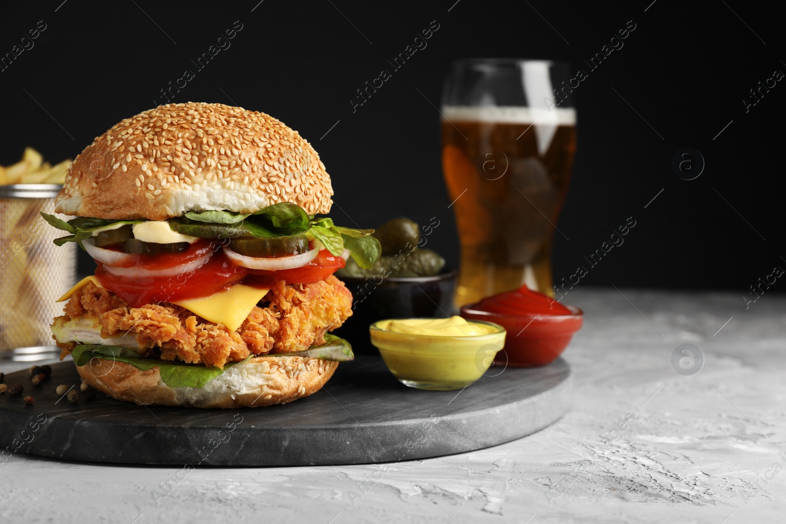 Photo of Delicious burger with crispy chicken patty and sauces on grey table