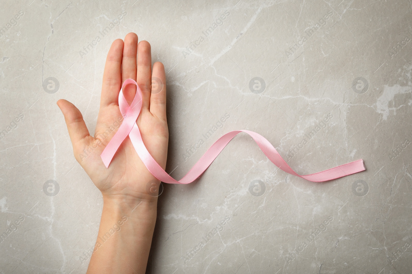 Photo of Woman holding pink ribbon on grey background, top view with space for text. Breast cancer awareness concept