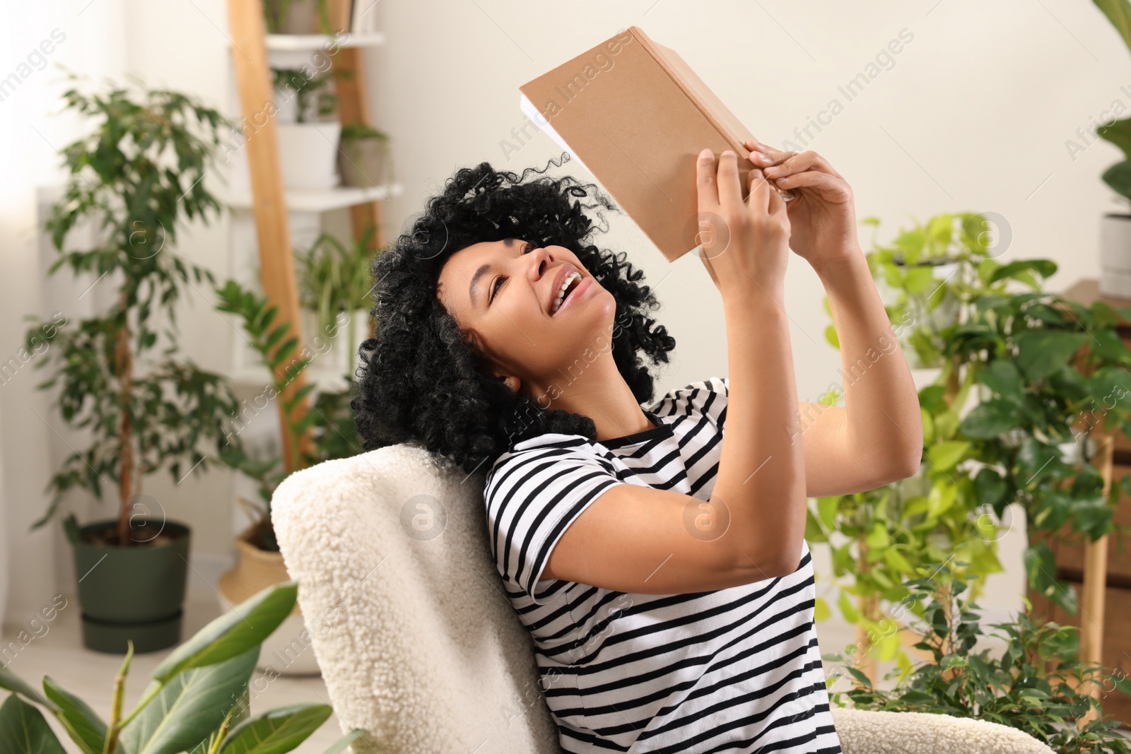 Photo of Relaxing atmosphere. Happy woman enjoying reading book near houseplants at home