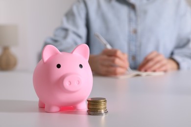 Photo of Woman at white table, focus on pink piggy bank. Space for text