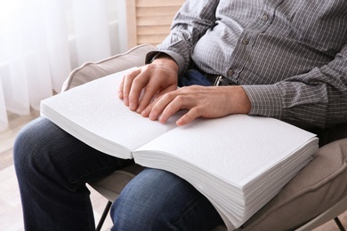 Blind man reading book written in Braille at home, closeup