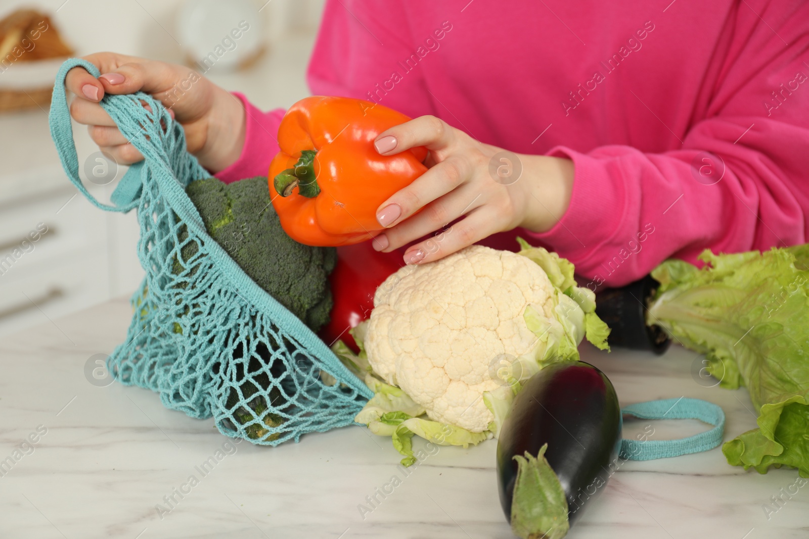 Photo of Woman taking pepper out from string bag at light marble table, closeup