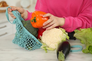 Woman taking pepper out from string bag at light marble table, closeup