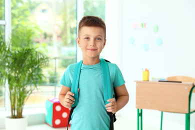 Cute little boy with backpack in classroom at school