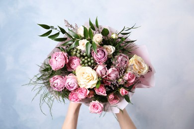 Photo of Woman with bouquet of beautiful roses on light blue background, closeup