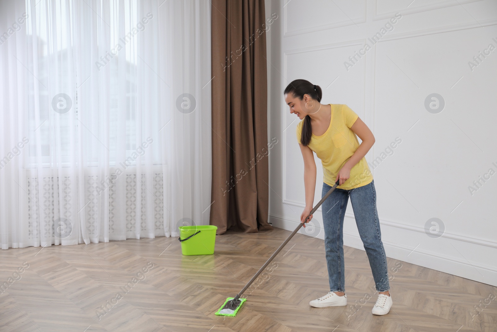 Photo of Young woman cleaning floor with mop in empty room