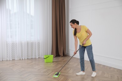 Young woman cleaning floor with mop in empty room