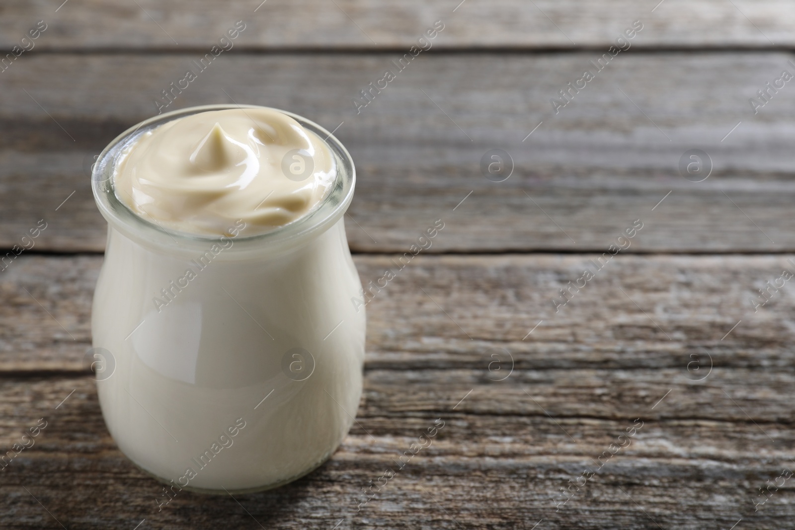 Photo of Fresh mayonnaise sauce in glass jar on wooden table, space for text