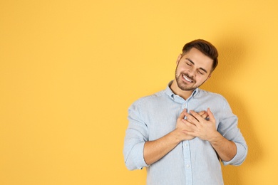 Portrait of young man holding hands near heart on color background, space for text