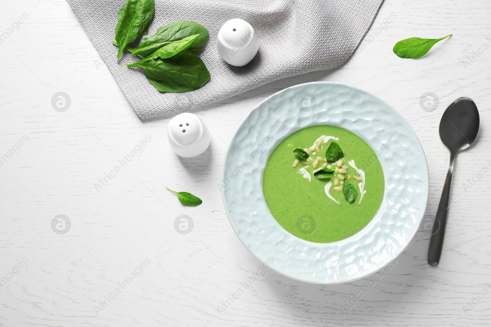 Photo of Plate of healthy green soup with fresh spinach served on white wooden table, flat lay. Space for text