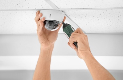 Photo of Technician installing CCTV camera on ceiling indoors, closeup