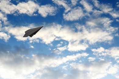 Image of Black paper plane flying in blue sky with clouds