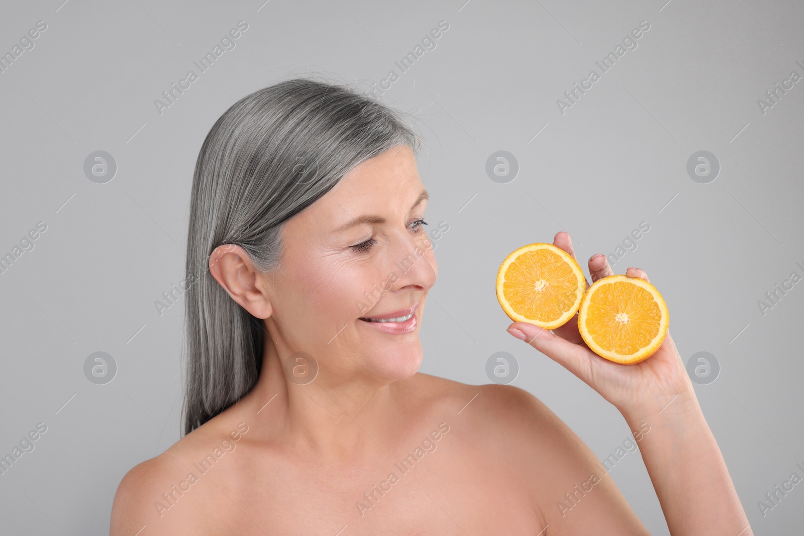 Photo of Beautiful woman with halves of orange rich in vitamin C on grey background