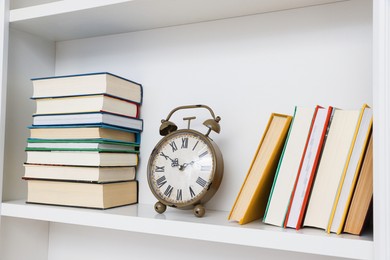 Photo of Different books and alarm clock on shelving unit