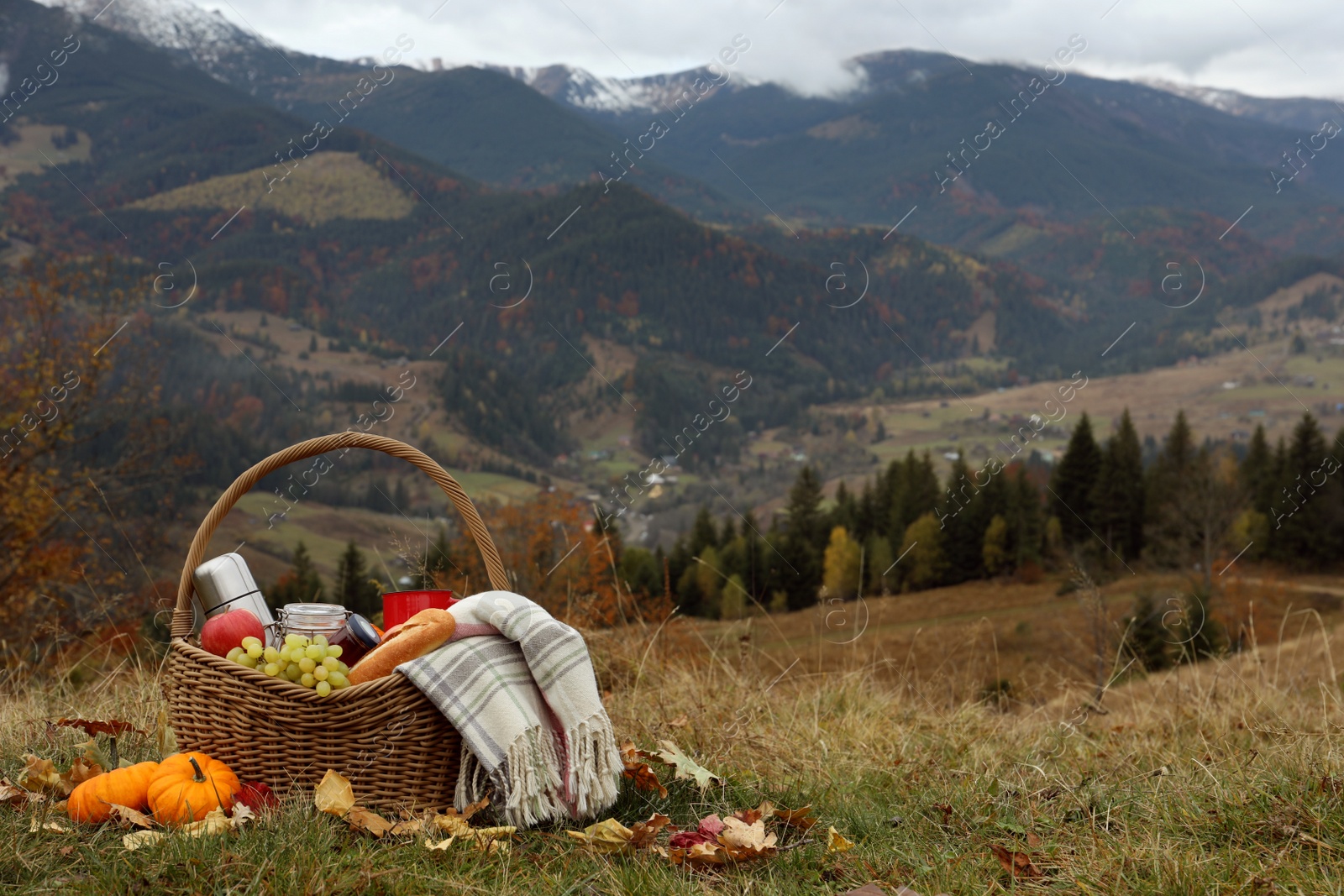 Photo of Wicker picnic basket with thermos, snacks and plaid in mountains on autumn day, space for text